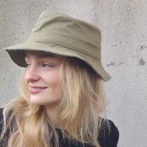 May include: A green canvas bucket hat with a wide brim. The hat is worn by a person with long blonde hair.
