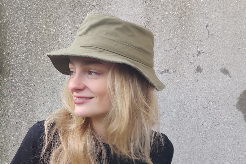 May include: A green canvas bucket hat with a wide brim. The hat is worn by a person with long blonde hair.