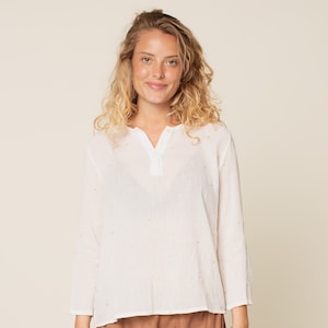 May include: A white, long-sleeved shirt with a button-up collar and a subtle pattern of small gold dots. The shirt is made of a lightweight fabric and has a relaxed fit.