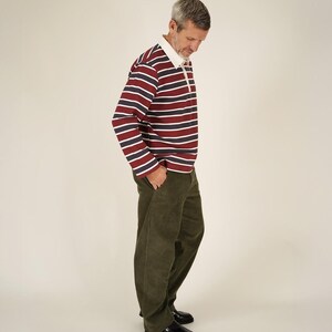 May include: A person wearing a rugby shirt with horizontal stripes in burgundy, navy, and white, paired with olive green corduroy pants and black leather shoes. The shirt has a white collar.