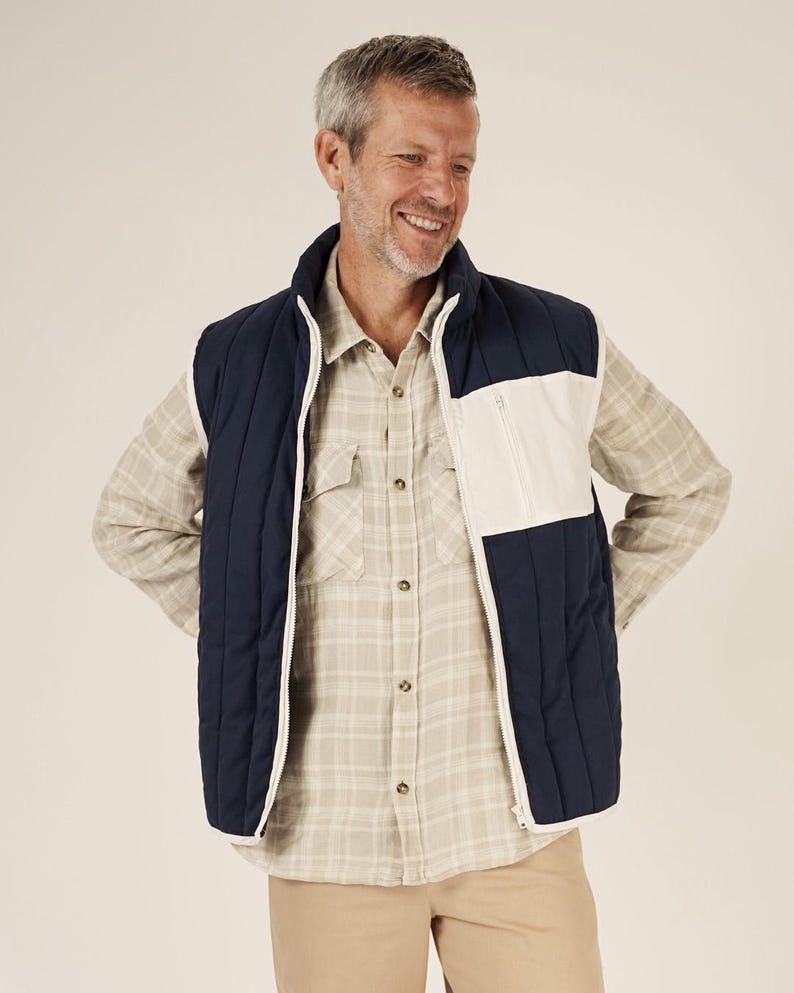 May include: A navy blue and white quilted vest with a full zipper closure. The vest has a white panel on the right side and a high collar. The person in the image is wearing a plaid shirt and khaki pants.