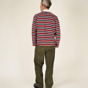 May include: A long-sleeved rugby shirt with horizontal stripes in burgundy, navy, and white, paired with olive green corduroy pants. The shirt has a white collar. The person is wearing black shoes.