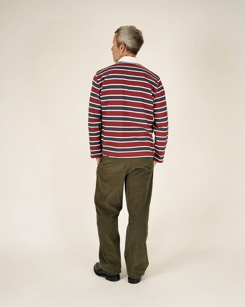 May include: A long-sleeved rugby shirt with horizontal stripes in burgundy, navy, and white, paired with olive green corduroy pants. The shirt has a white collar. The person is wearing black shoes.