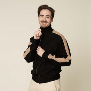 May include: A black zip-up jacket with tan colour block stripes on the sleeves and shoulders. The jacket has a mock neck and a zipper closure.