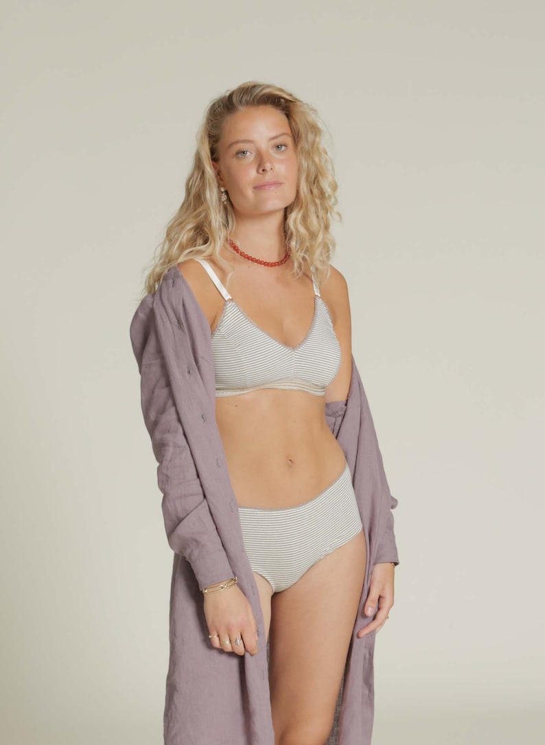 Puede incluir: Conjunto de sujetador y ropa interior a rayas claras. El sujetador tiene tirantes finos y un dise&ntilde;o de cuello en V. La ropa interior es de talle alto. Una camisa larga de color p&uacute;rpura claro est&aacute; drapeada sobre los hombros.