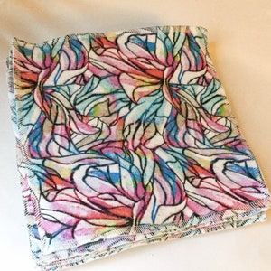 May include: A stack of colorful fabric squares with a stained glass pattern. The fabric is white with pink, blue, and yellow accents. The squares are sewn together with a white thread.