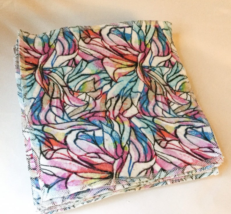 May include: A stack of colorful fabric squares with a stained glass pattern. The fabric is white with pink, blue, and yellow accents. The squares are sewn together with a white thread.