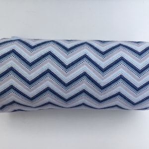 May include: A roll of blue and white chevron patterned fabric with white polka dots. The fabric is rolled up and has a white background.