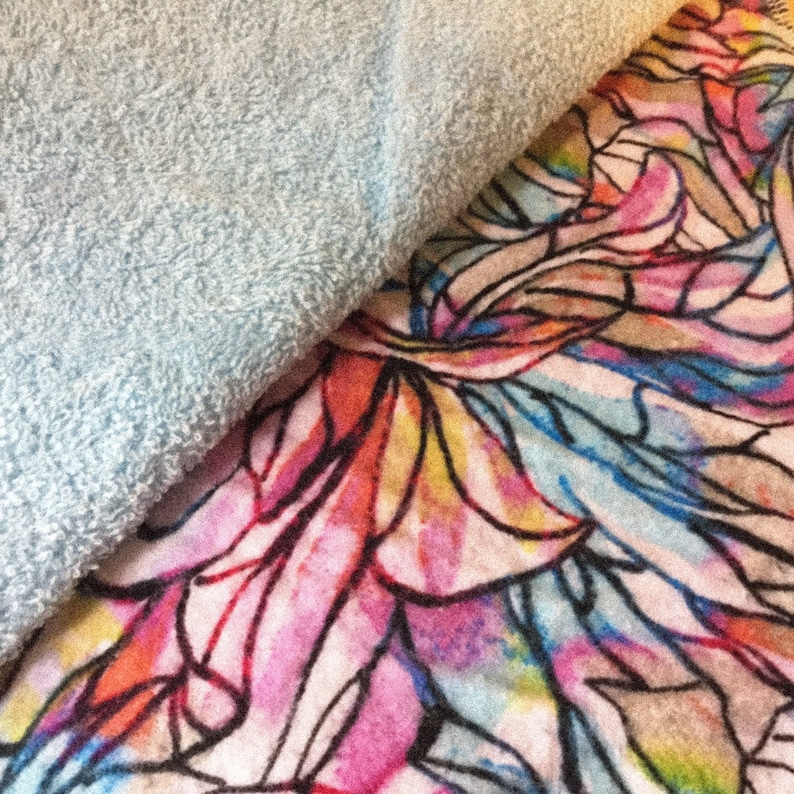 May include: A close-up of a soft, blue, fuzzy fabric overlapping a colorful fabric with a floral pattern. The floral pattern is a watercolor style with pink, blue, yellow, and orange hues.