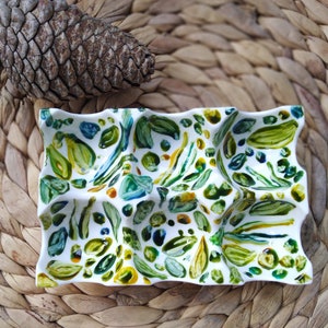 May include: A white ceramic dish with a wavy edge and a green, blue, and yellow abstract design. The dish is divided into sections.