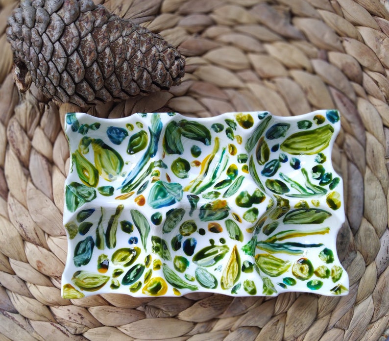 May include: A white ceramic dish with a wavy edge and a green, blue, and yellow abstract design. The dish is divided into sections.