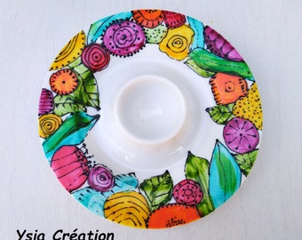 Puede incluir: Un huevo de cerámica blanca con un diseño floral colorido. El diseño presenta flores y hojas de color amarillo brillante, naranja, rojo, rosa, verde y azul. El huevo es perfecto para servir un solo huevo.