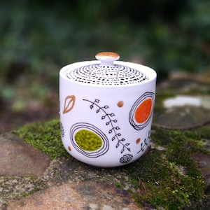 May include: White ceramic sugar bowl with a lid. The bowl has a black and white geometric pattern with orange and green accents.