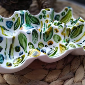 May include: White ceramic egg holder with a wavy design and painted with green, blue, and yellow abstract shapes.