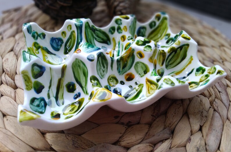May include: White ceramic egg holder with a wavy design and painted with green, blue, and yellow abstract shapes.
