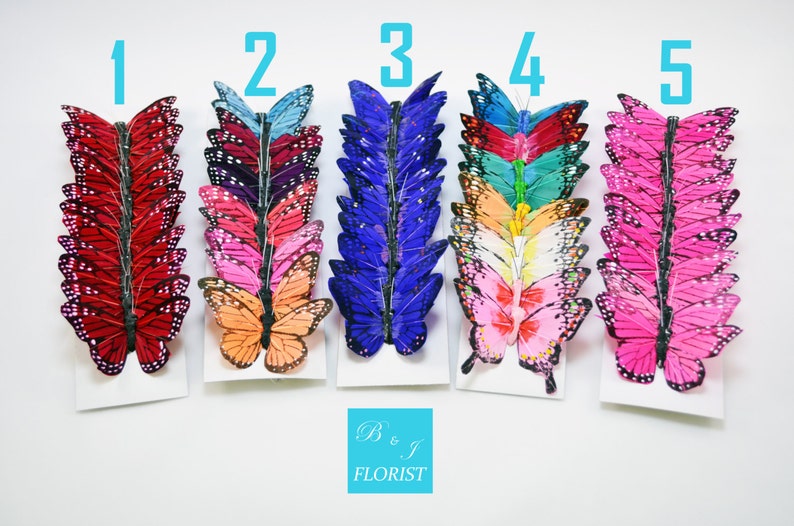 Pode incluir: Cinco filas de enfeites de borboleta coloridos, cada fila com um esquema de cores diferente. As borboletas est&atilde;o dispostas em linha vertical, com a borboleta superior voltada para cima e a borboleta inferior voltada para baixo. As cores incluem vermelho, rosa, azul, verde e roxo.