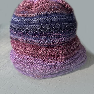 Peut inclure: Un bonnet tricoté rayé violet, rose et bleu avec une coupe ample.