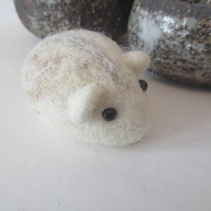 May include: A small, white, felted mouse with black eyes. The mouse is sitting on a white surface.