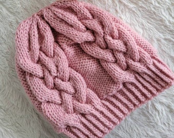 May include: A pink knitted hat with a cable knit pattern. The hat is made with a soft yarn and has a cozy feel.