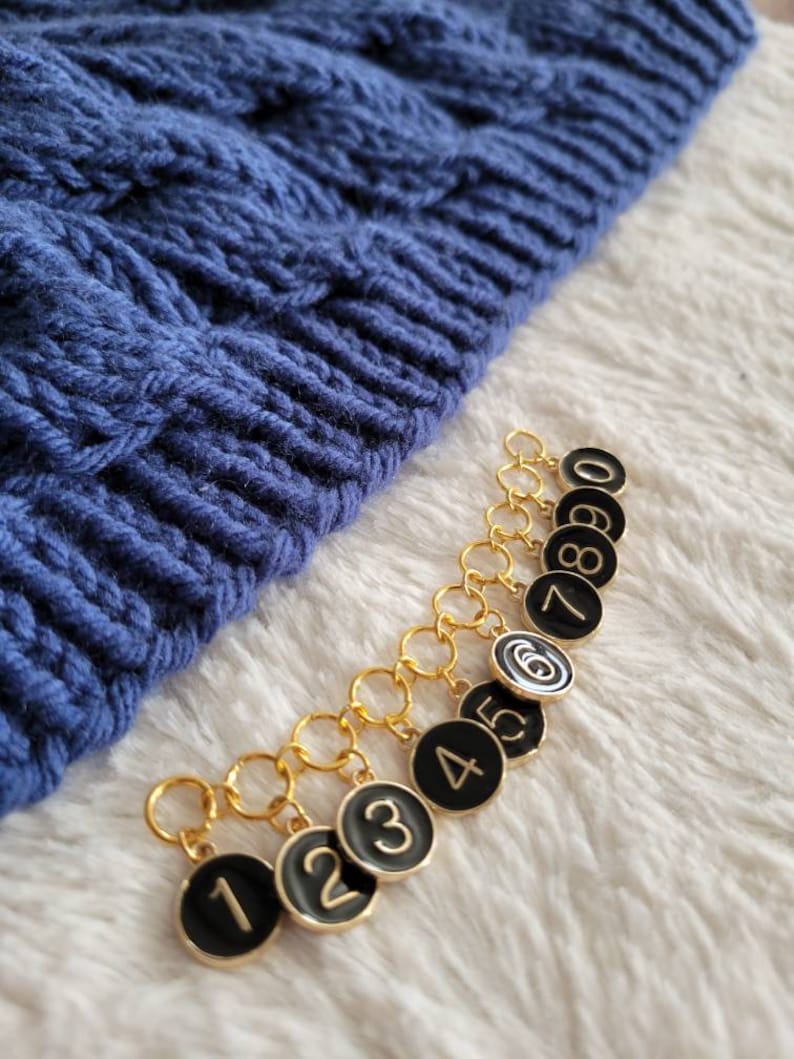 May include: A set of ten gold stitch markers with black round tags numbered 1 through 8 and 0. The tags have gold numbers.