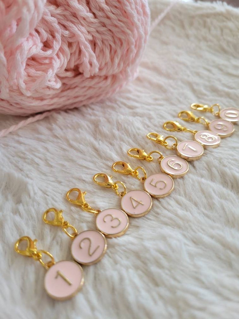 May include: Ten gold-colored stitch markers with pink round discs numbered 1 through 10. The markers have a spring-loaded clasp.