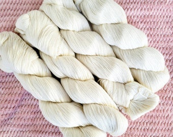 Puede incluir: Cuatro ovillos de hilo blanco, dispuestos en forma de cruz, sobre una superficie de crochet rosa.