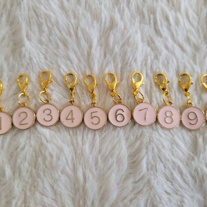 May include: Ten gold-colored stitch markers with pink enamel and white numbers 1 through 10.