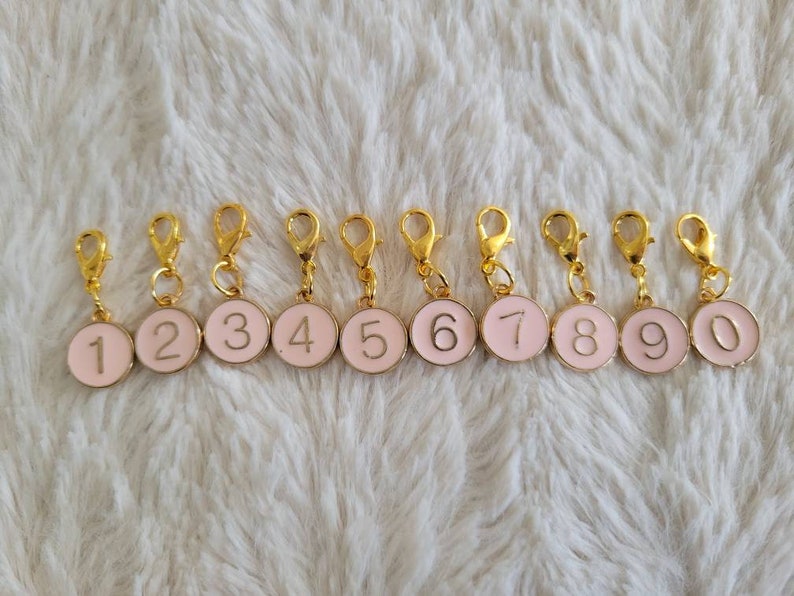 May include: Ten gold-colored stitch markers with pink enamel and white numbers 1 through 10.