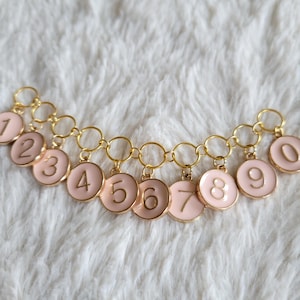 May include: A gold chain with ten pink circular charms, each with a gold number from 1 to 10.