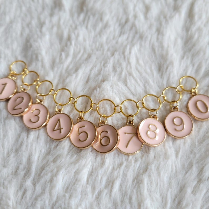 May include: A gold chain with ten pink circular charms, each with a gold number from 1 to 10.
