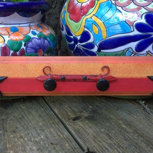 May include: A wooden coat rack with a red, orange and yellow paint design. It has two black metal hooks with star-shaped accents. The rack is decorated with two black metal knobs.