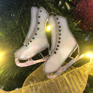 May include: White glass ice skate ornament with black accents hanging on a gold ribbon on a Christmas tree.