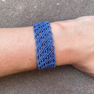 Può includere: Un braccialetto in macramè blu con un design intrecciato. Il braccialetto è di colore blu unito e sembra fatto a mano. Il braccialetto è largo circa 3,8 cm.