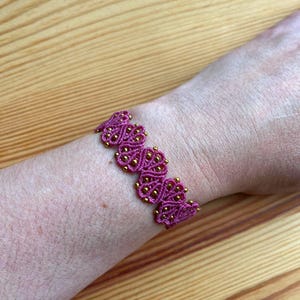 Könnte beinhalten: Ein rosa und goldenes Armband mit einem Herzdesign.