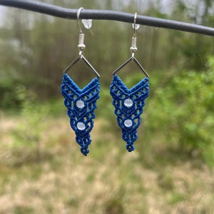 May include: A pair of blue macrame earrings with white beads hanging from silver hooks.