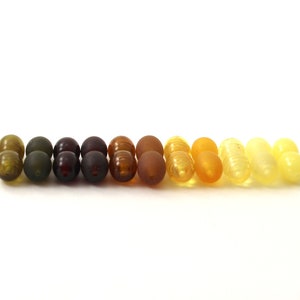 May include: A row of amber beads in various shades of green, brown, and yellow.