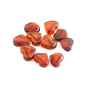 May include: A group of ten heart-shaped amber beads. The beads are a deep orange-red color and have a translucent finish.
