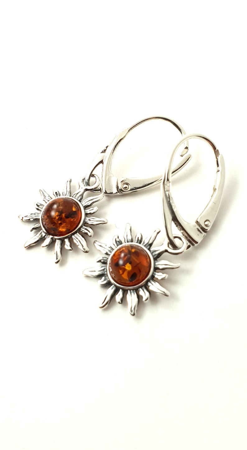 May include: A pair of silver earrings with amber sun pendants. The earrings have a hook closure.