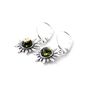 May include: A pair of silver earrings with green amber stones set in a sunburst design. The earrings have a hook closure.