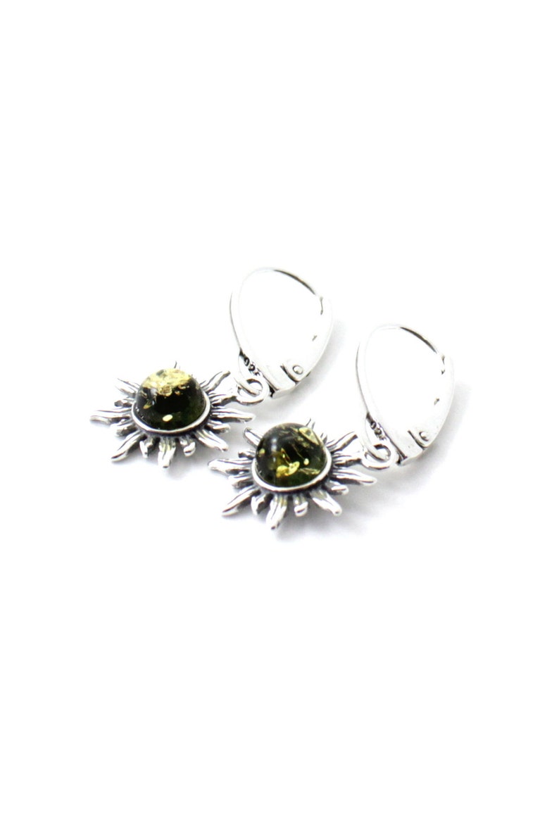 May include: A pair of silver earrings with green amber stones set in a sunburst design. The earrings have a hook closure.