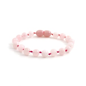 Könnte beinhalten: Ein Armband aus rosa Rosenquarz mit roter Schnur. Das Armband besteht aus runden Perlen und hat einen geknoteten Verschluss.