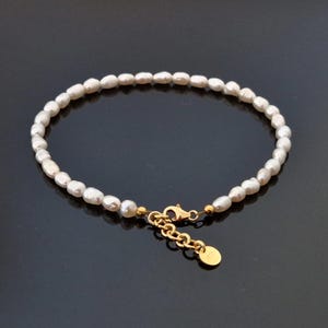 Puede incluir: Un delicado brazalete de perlas blancas con cierre y cadena extensora de oro. El brazalete está hecho de pequeñas perlas redondas y tiene un diseño simple y elegante.