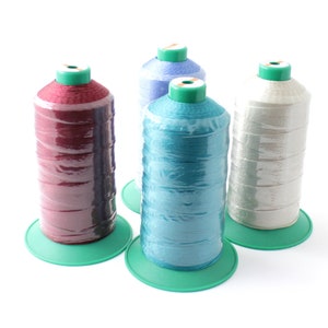 May include: Four spools of thread on green bases. The spools are wrapped in red, blue, light blue, and white thread.