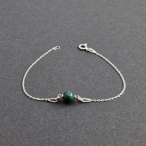 May include: A silver chain bracelet with a single green gemstone bead.