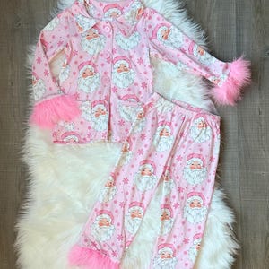 May include: Pink pyjamas with a Santa Claus print and fluffy pink trim on the cuffs.