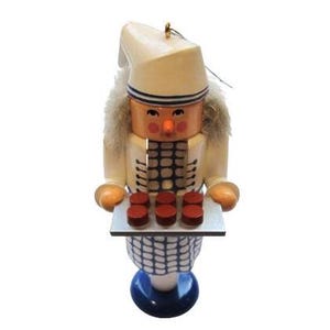 May include: A wooden nutcracker figurine wearing a white hat and blue and white patterned clothing. The nutcracker is holding a tray of red and white cookies.