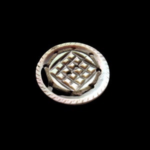 May include: A round, white, mother-of-pearl button with a carved geometric design.