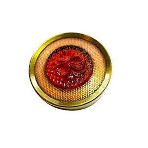 May include: A round, antique-style button with a gold-colored metal rim. The button features a red, textured center with a detailed design, set within a mesh-like pattern. The button is isolated on a white background.