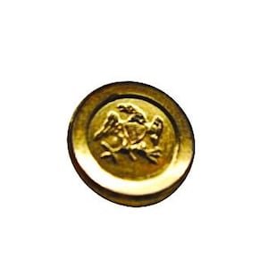 May include: A gold-colored button with a raised design of an eagle holding a shield. The button has a circular shape and a slightly raised edge. The eagle is the central focus of the design.