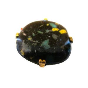 May include: A vintage brooch with a dark, speckled, oval-shaped stone. The stone has flecks of yellow, teal, and white against a black background. The brooch is accented with gold-toned metal details.